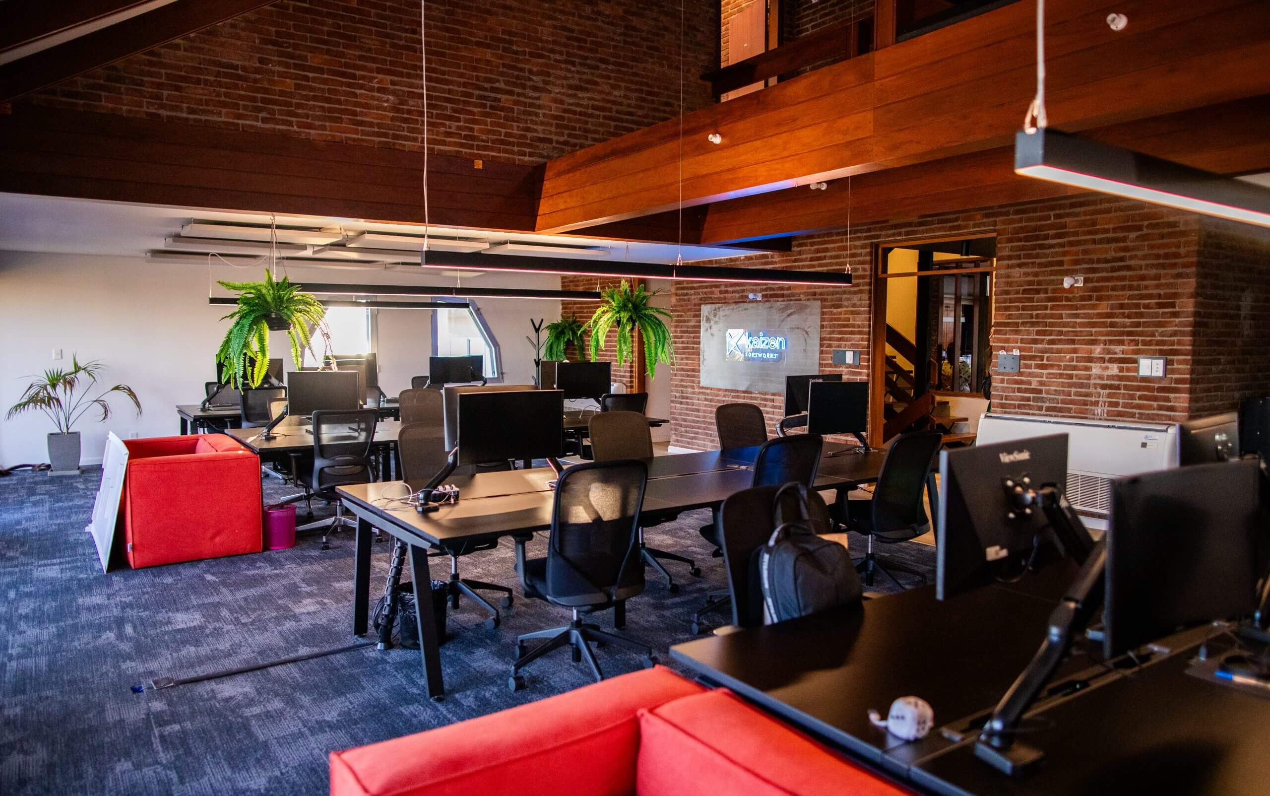 Inside Kaizen Softworks' dynamic open office space, illuminated by the glow of computer screens and a distinctive neon sign showcasing the company logo.